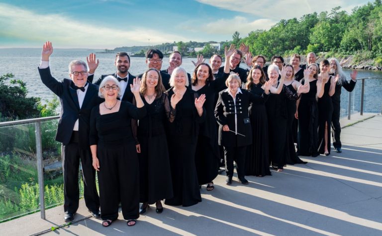 The Elmer Iseler Singers posing for a photo on a deck overlooking the lake.